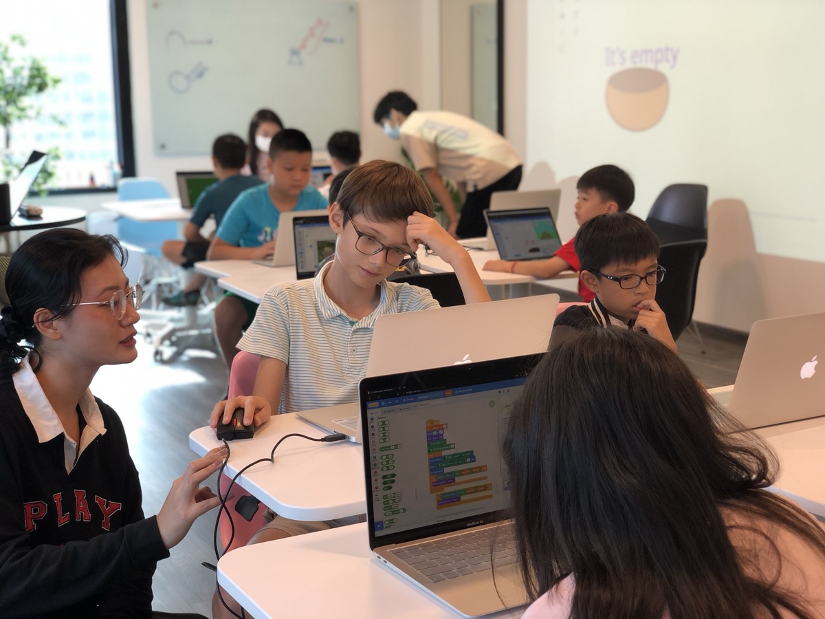 An LCCL teacher sitting beside students at their laptops, guiding them through a Scratch project